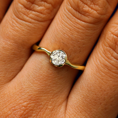 Close up view of a model's hand wearing a 14k yellow gold round lab clear diamond liquid ring