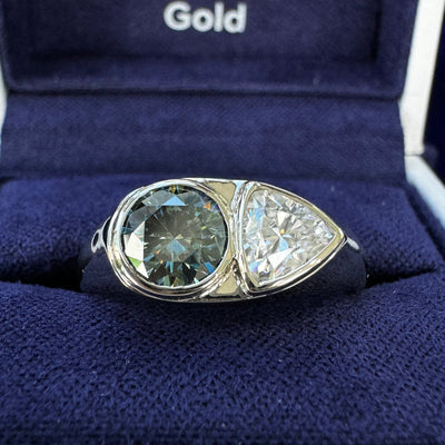 A photo of 14k Champagne Gold 6.5mm Round Gray Blue Moissanite with 6.5mm Trillion White Moissanite Custom Signet Ring in a blue ring box