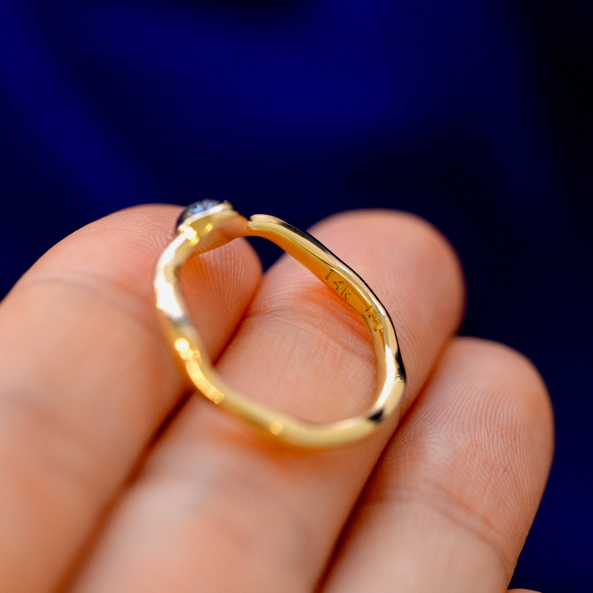 A solid gold round cabochon salt and pepper diamond ring on a model's fingertips showing all the curves in the band