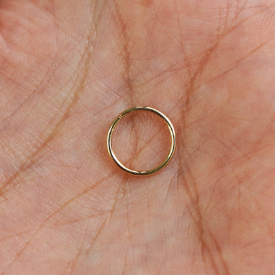 A model's hand holding a 14 karat yellow gold Pierced Line Septum