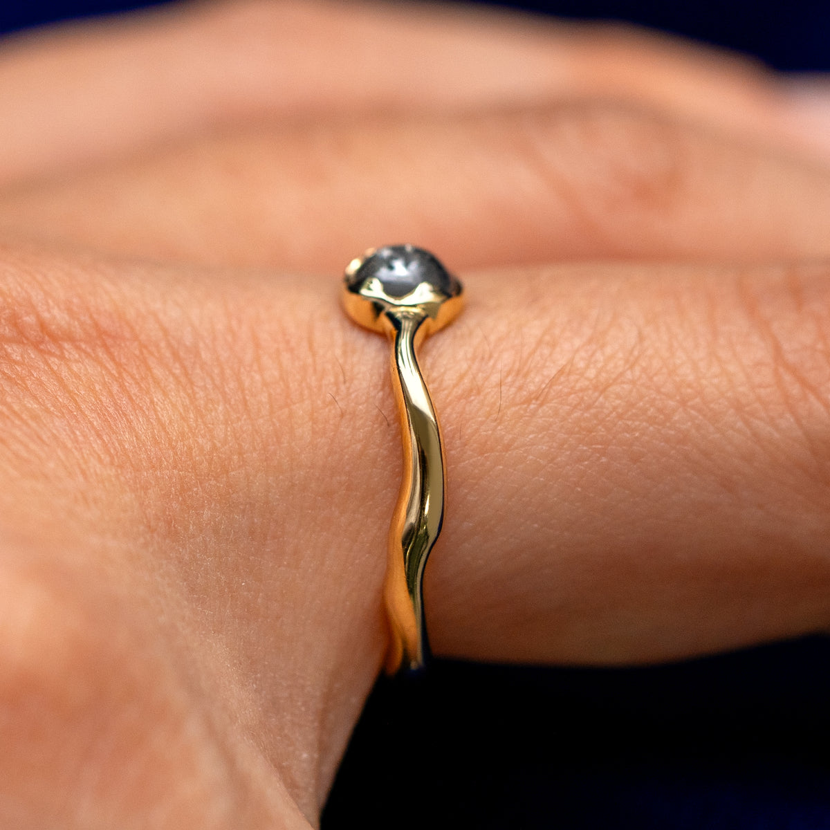 Side view of a solid 14 karat gold round cabochon salt and pepper diamond engagement ring on a model's finger