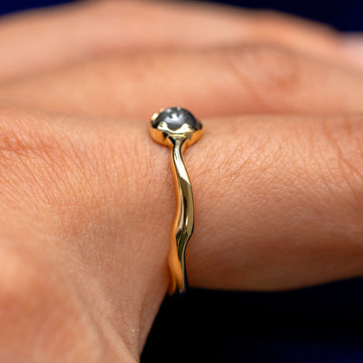 Side view of a solid 14 karat gold round cabochon salt and pepper diamond engagement ring on a model's finger