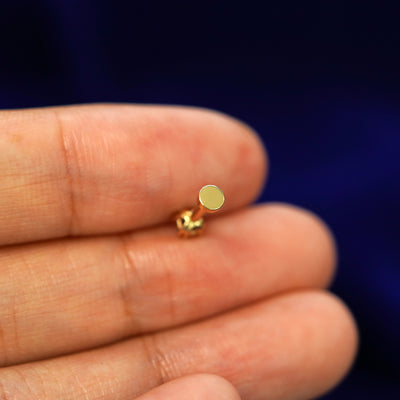 A solid yellow gold Ruby Flatback Piercing laying facedown on a model's finger to show the end of the flat back