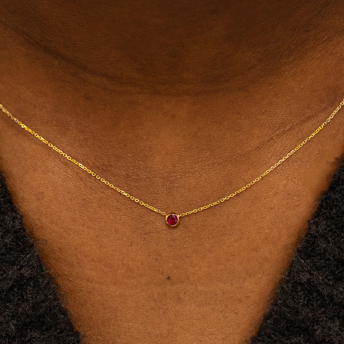 Close up view of a model neck wearing a 14k yellow gold Bezel set Ruby gemstone necklace 