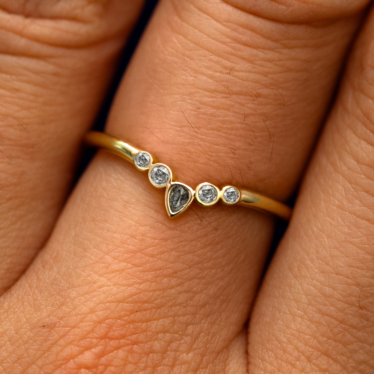 Close up view of a model's fingers wearing a 14k yellow gold Chevron Tiara Salt and Pepper Diamond Band
