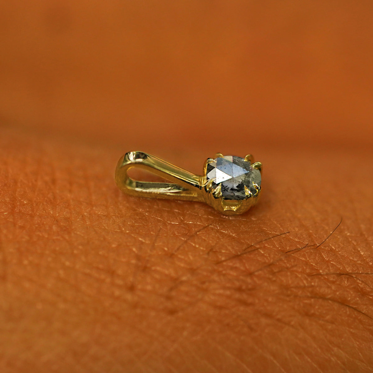 A 14k yellow gold Salt and Pepper Diamond Charm for chain resting on the back of a model's hand