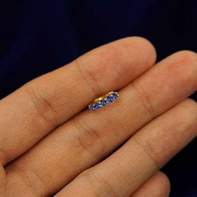 A small Blue Sapphire huggie hoop earring between a model's fingers to show the gems