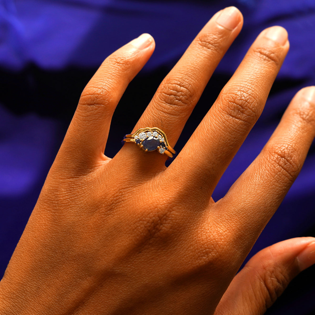 Close up view of a model's hand wearing a yellow gold Sapphire and Diamond Cluster Ring Set