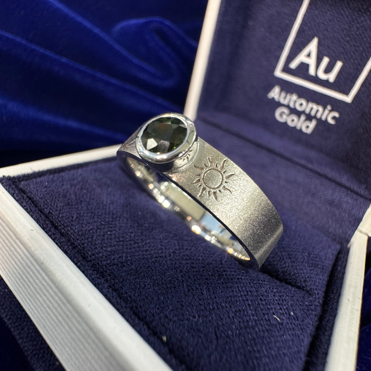 14k White Gold Bezel-set 5mm Green Sapphire w/ Sun & Crescent Moon Engravings on 5mm Matte Industrial Band Custom Ring in a blue ring box