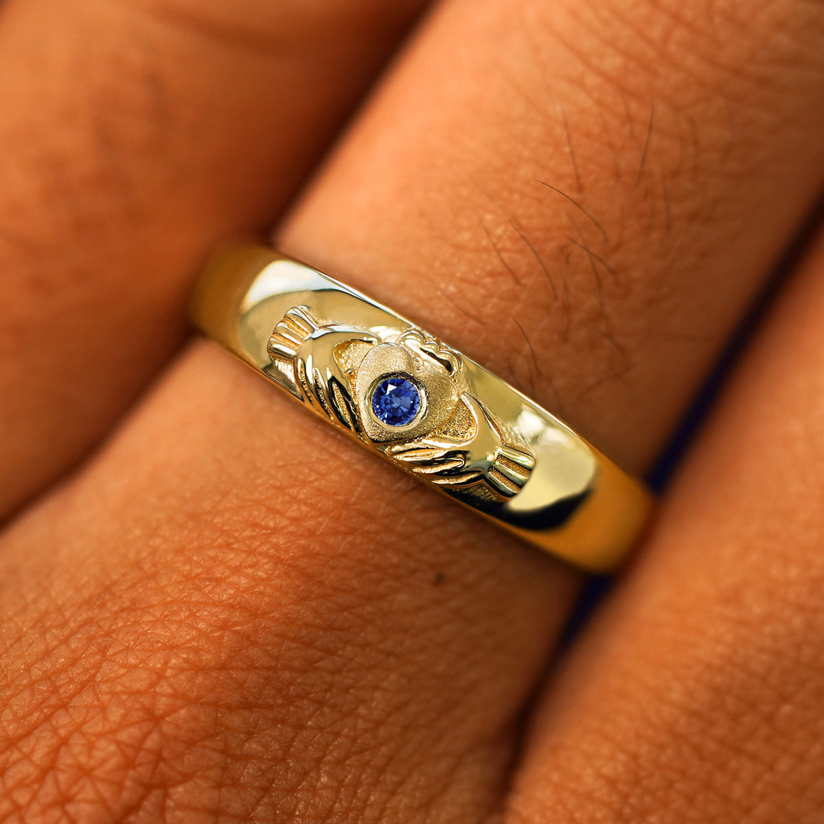 Close up view of a model's fingers wearing a 14k yellow gold blue sapphire Gemstone Claddagh Band
