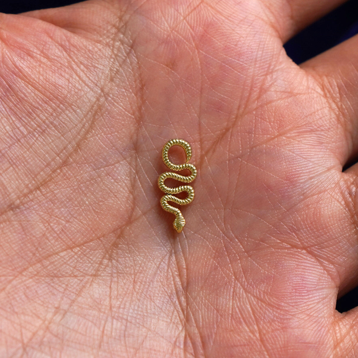 A solid gold Snake Charm for earring resting in a model's palm to show the underside of the charm