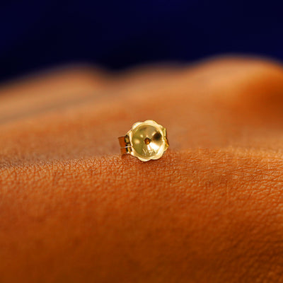 A single solid 14k gold large push back earring backing on the back of a hand