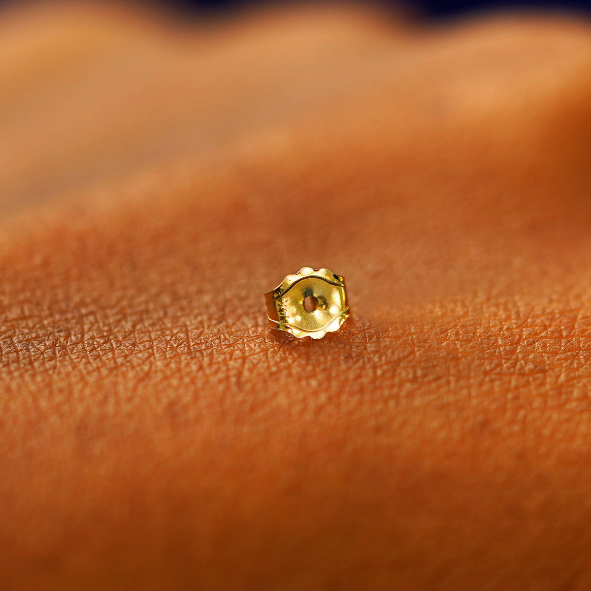 A single solid 14k gold standard push back earring backing on the back of a hand