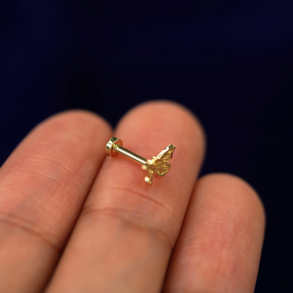 Alternate side view of a Mini Butterfly Flat back piercing sitting on a model's fingertips