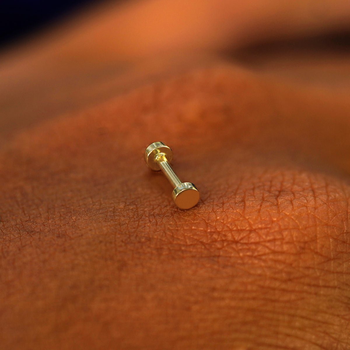 A solid 14k yellow gold Small Circle Flatback Piercing resting on the back of a model's hand