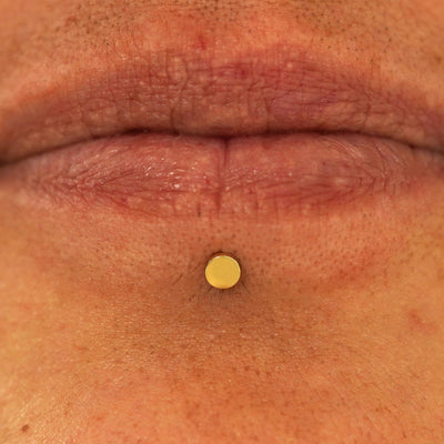 Close up view of a model's lips wearing a 14k yellow gold Small Circle Flatback in a labret piercing