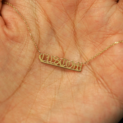 A small 14k yellow gold custom nameplate necklace resting in a model's palm