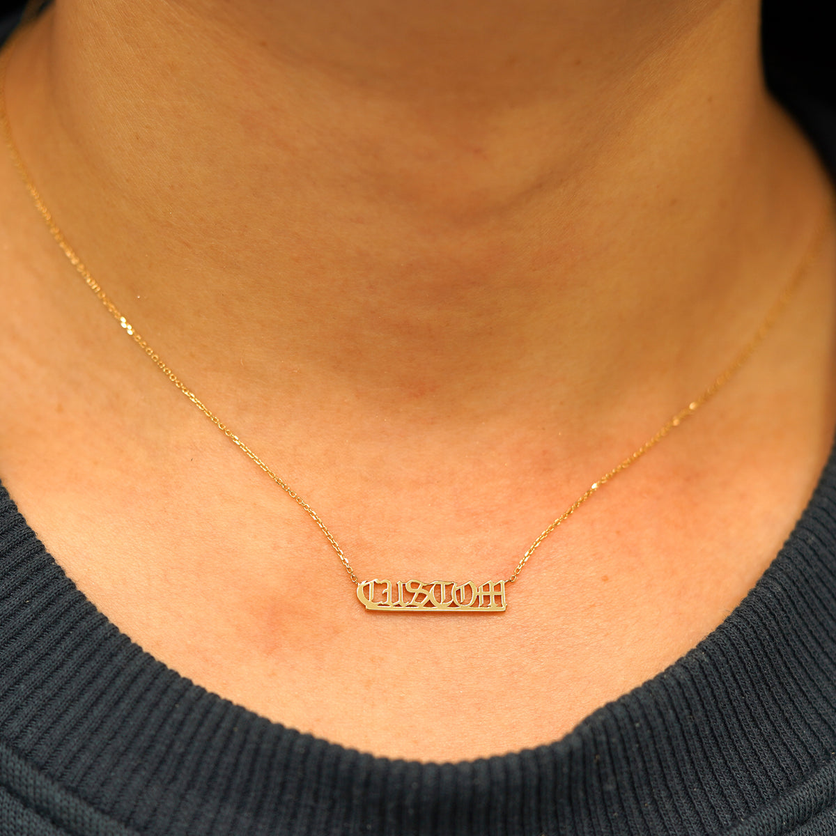 A model's neck wearing a Small Custom Nameplate necklace that reads the word Custom