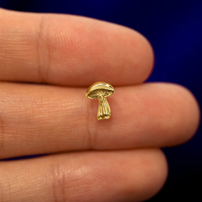 A model holding a solid gold Mushroom stud earring between two fingers