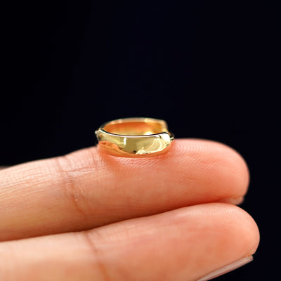 A yellow gold Small Thick Huggie Hoop Earring laying sideways on a model's fingertips