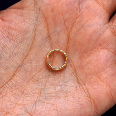 A solid 14k yellow gold Small Thick Huggie Hoop Earring closed in a model's palm