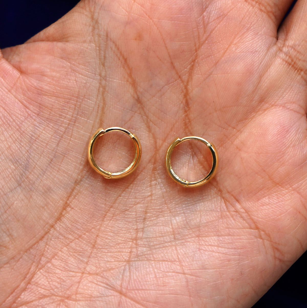 A pair of 14k gold Small Thick Huggie Hoop Earring sitting in a model's palm