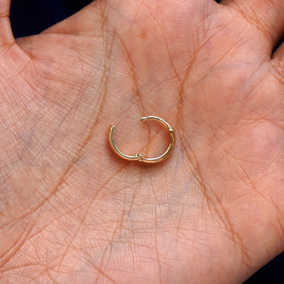 A solid 14k yellow gold Small Thick Huggie Hoop Earring open in a model's palm to show the hinge