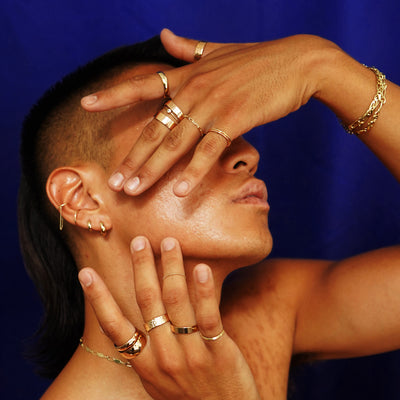 A model with head tilted up and their hands raised over their face wearing various Automic Gold jewelry