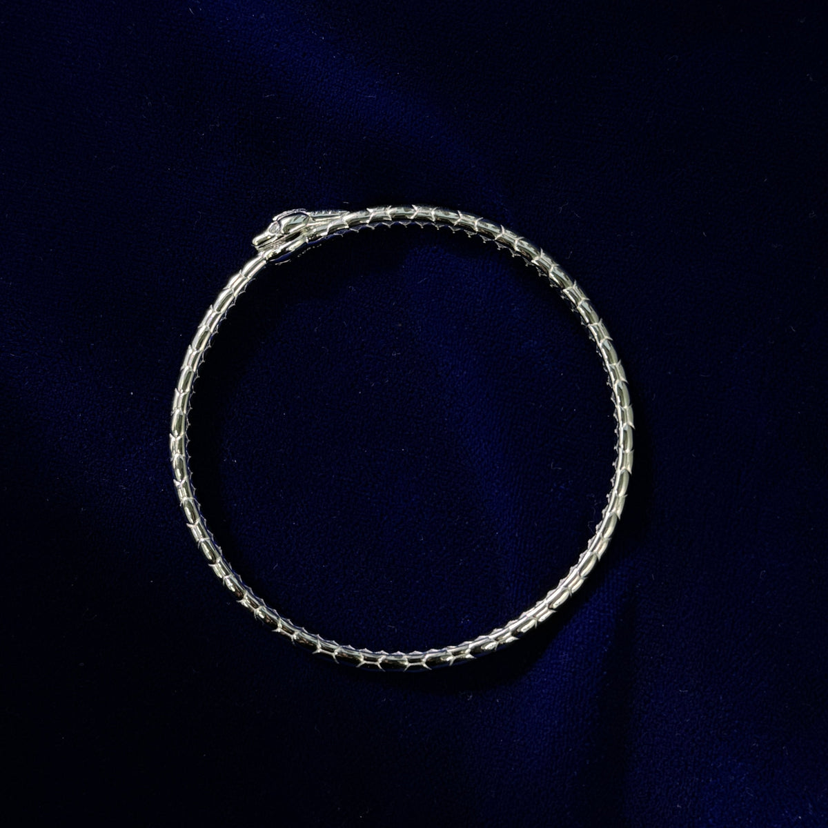 A solid platinum and diamond Ouroboros snake bracelet on a dark blue cloth background