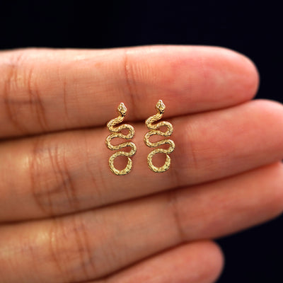 A model's hand holding a pair of recycled 14k gold Snake Earrings