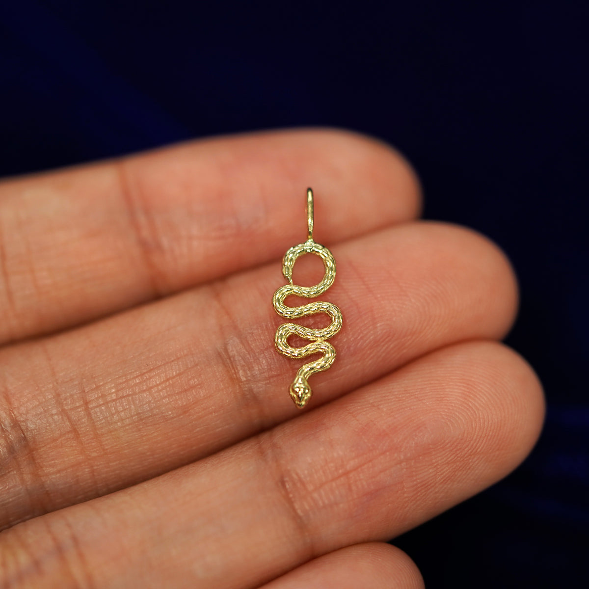 A 14k yellow gold Snake Charm with a bail for a chain resting on a model's fingertips
