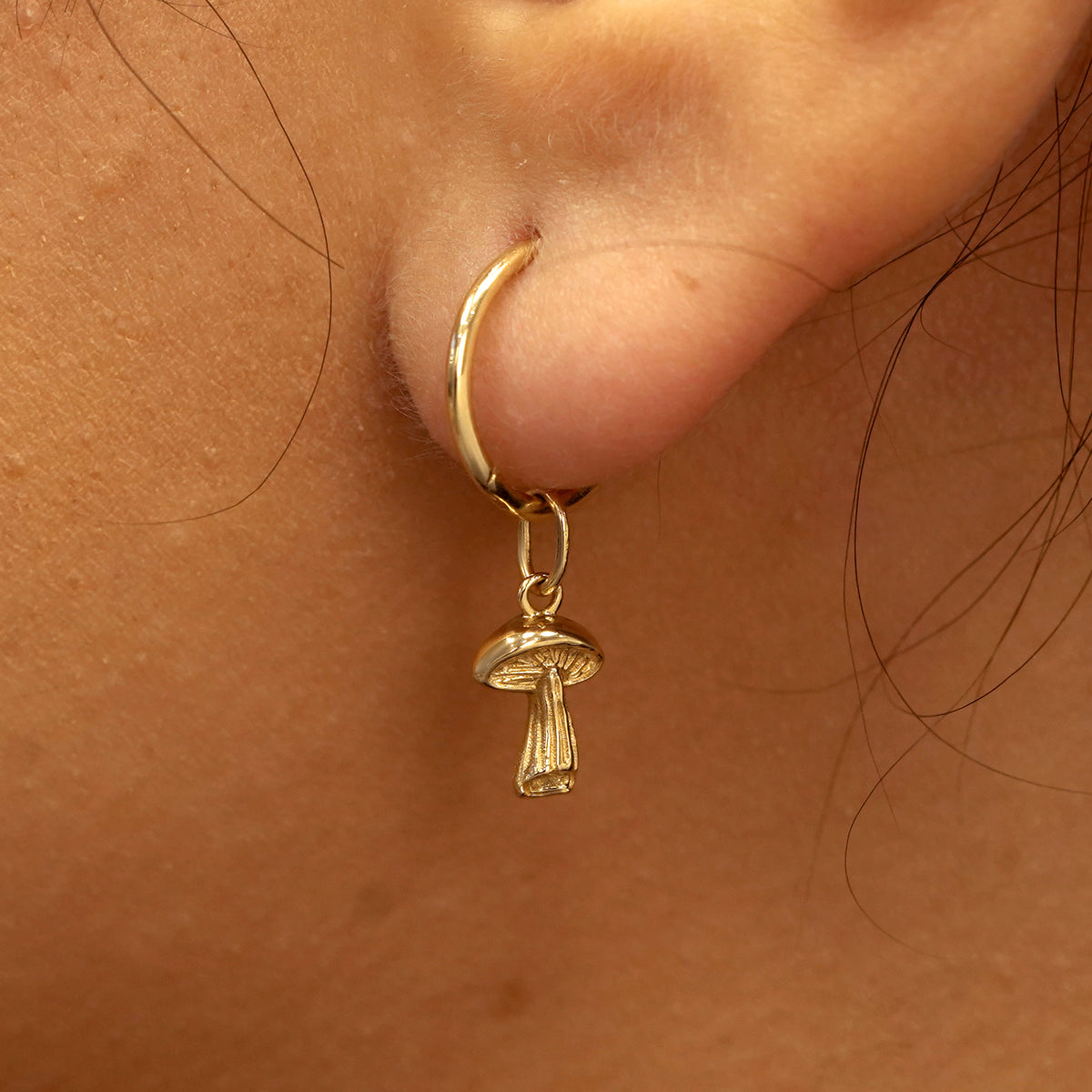 Close up view of a model's ear wearing a yellow gold Mushroom Charm on a Small Seamless Huggie Hoop