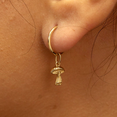 Close up view of a model's ear wearing a yellow gold Mushroom Charm on a Small Seamless Huggie Hoop