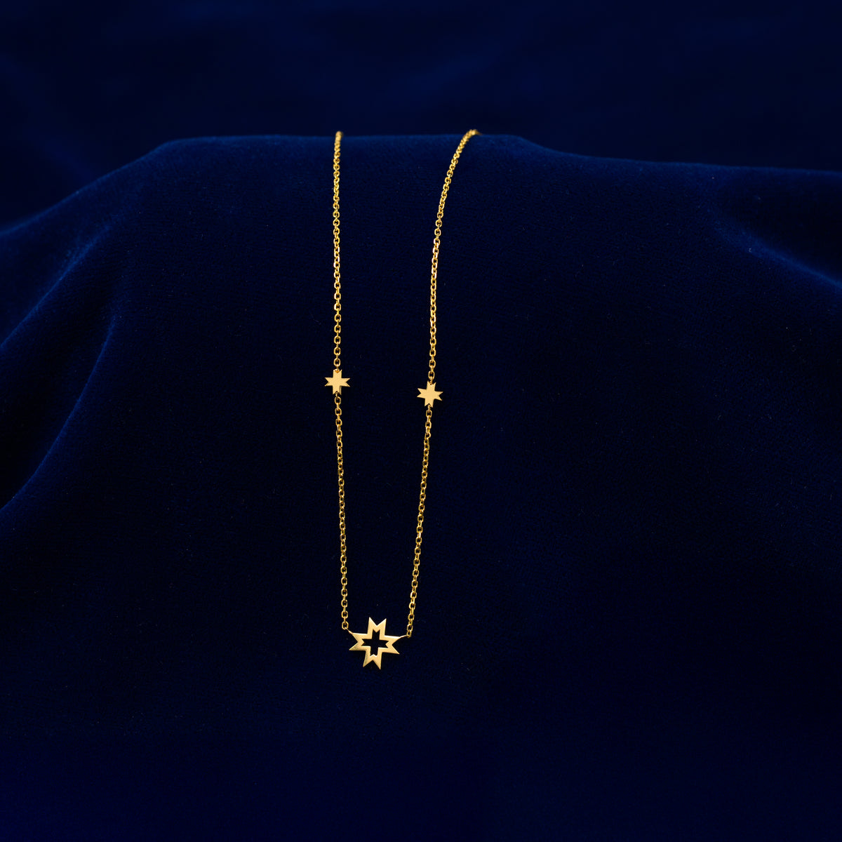 A solid gold 8 pointed star necklace draped across a dark blue cloth