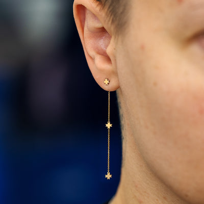A model wearing a 14k yellow gold 8 pointed star extender with an 8 pointed star stud earring