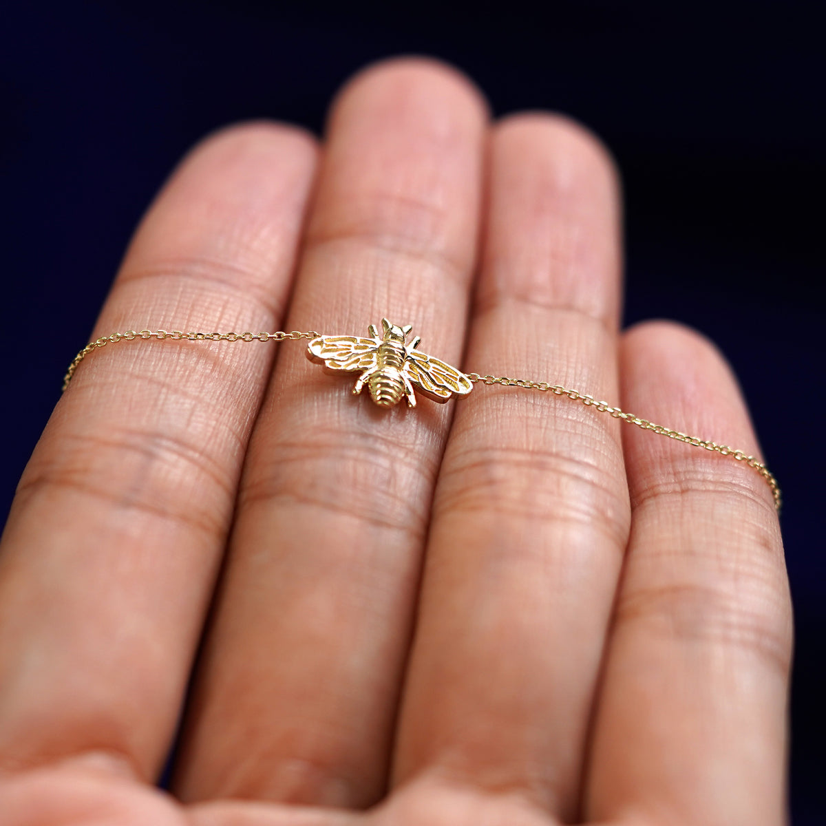 A yellow gold Bee Necklace resting on a model's fingers
