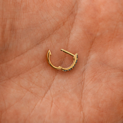 An open blue sapphire huggie hoop laying in a models palm