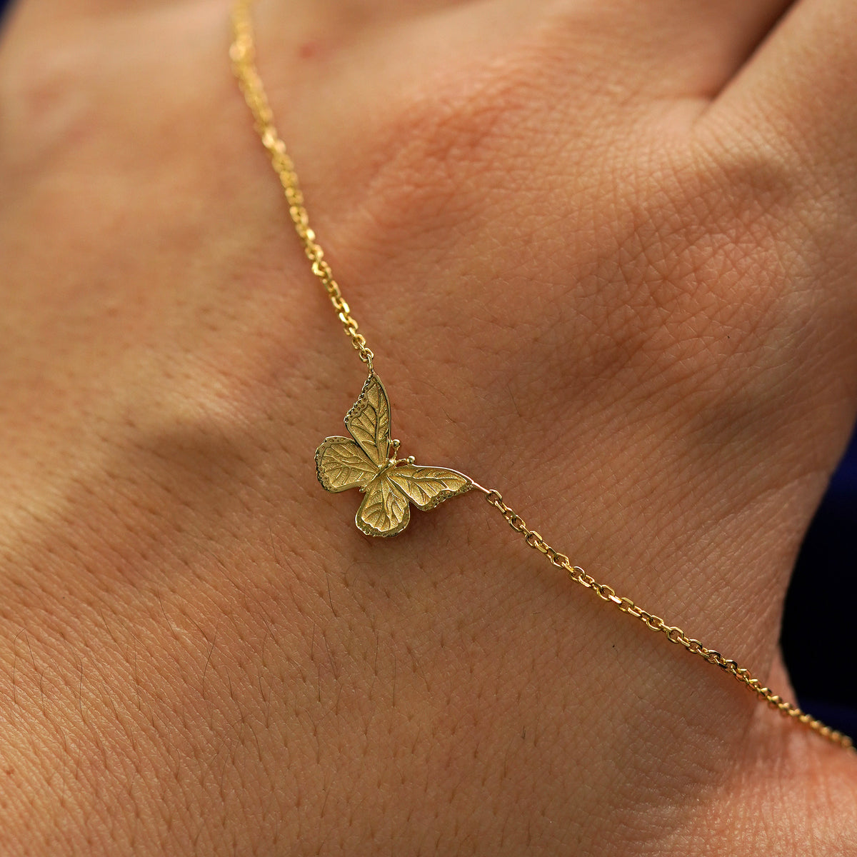 A solid gold butterfly necklace draped across the back of a model's hand