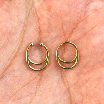 Two 14k gold Double Circle Septum rings show in options of Non-Pierced and Pierced resting in the palm of a model's hand
