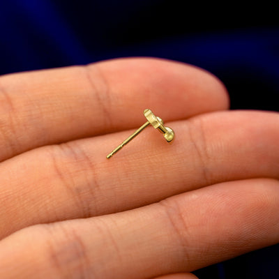 A 14k gold Cherry Earring in a model's hand resting on its side to show the thickness of the earring 