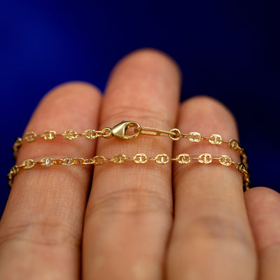 A yellow gold Flat Mariner Chain Anklet wrapped around a model's fingers to show the chain and the lobster claw clasp