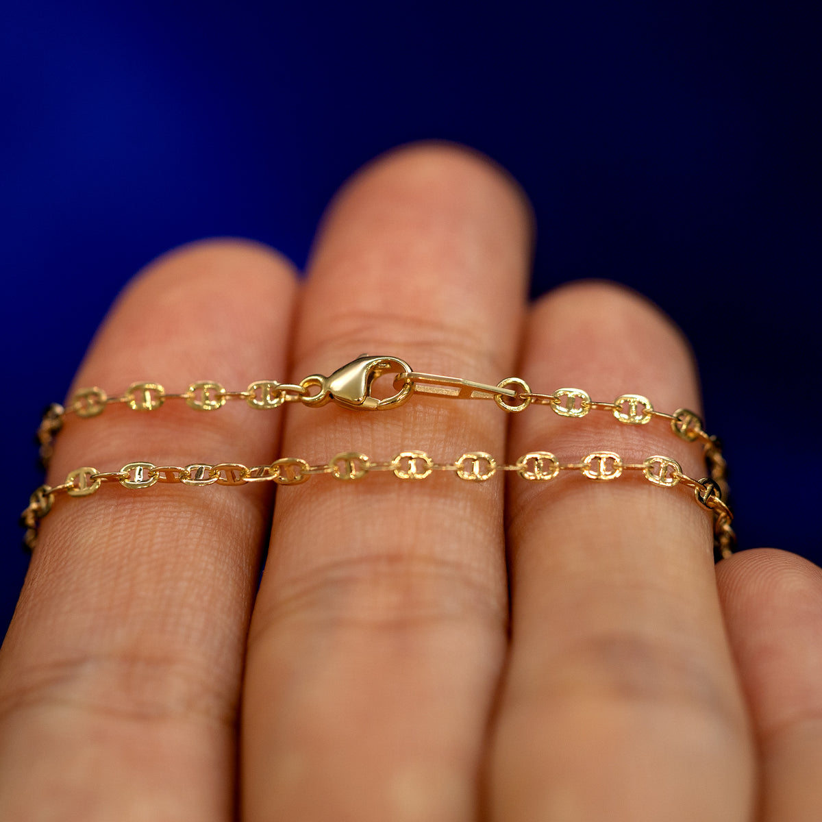 A yellow gold Flat Mariner Chain Necklace wrapped around a model's fingers to show the chain and the lobster claw clasp