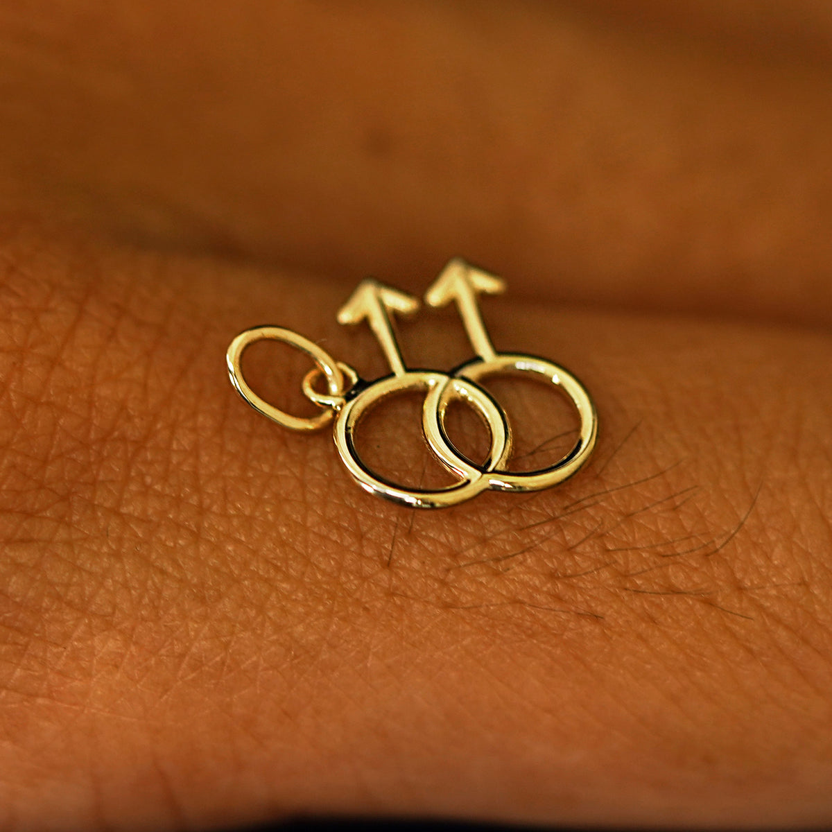 A 14k solid gold Gay Symbol Charm for chain balancing on the back of a model's finger