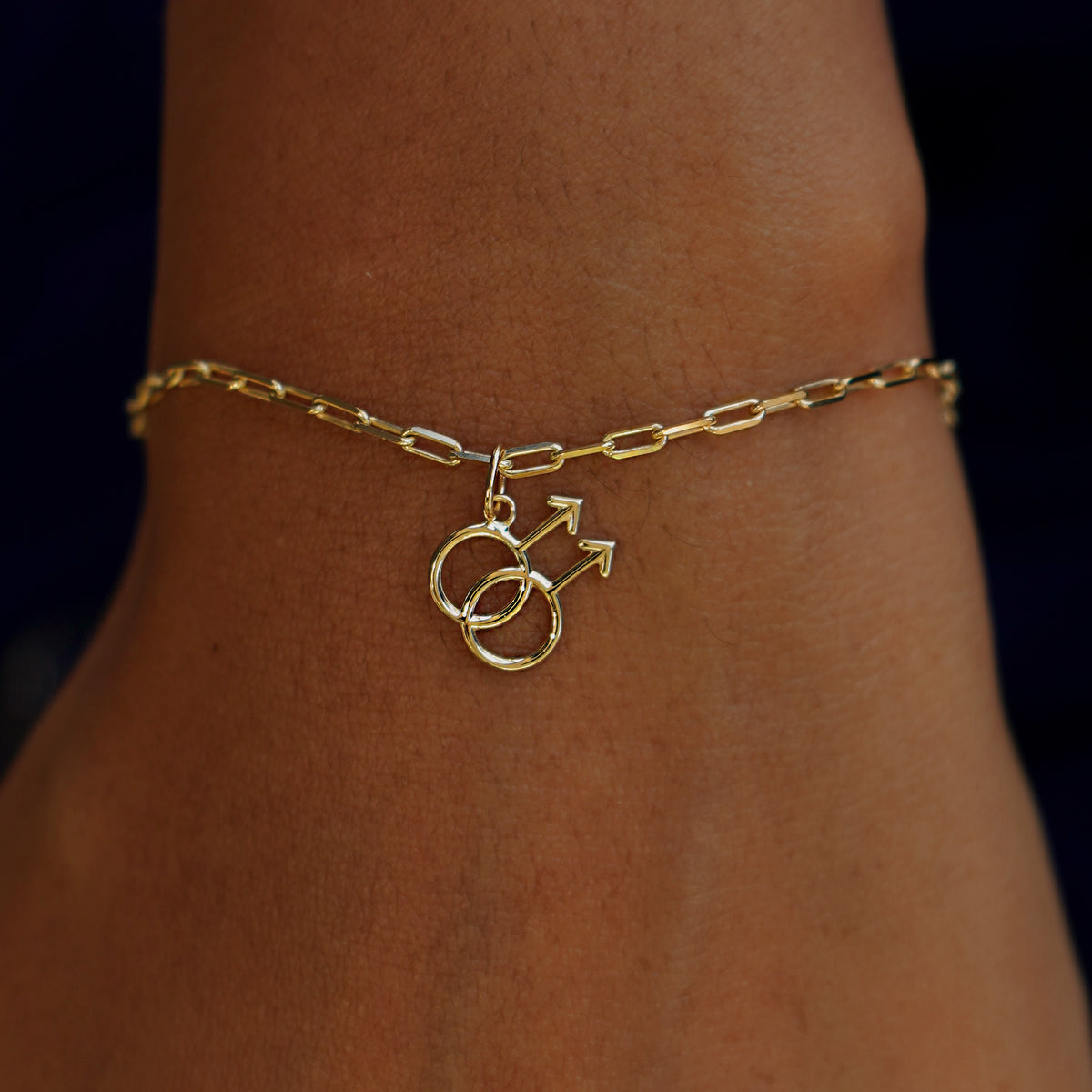 A model's wrist wearing a yellow gold Gay Symbol Charm on a Butch Bracelet