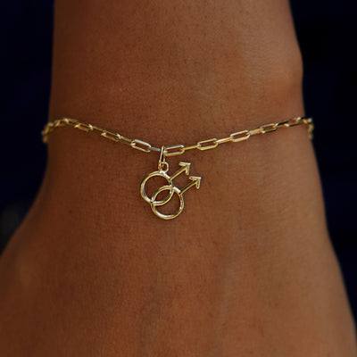 A model's wrist wearing a yellow gold Gay Symbol Charm on a Butch Bracelet