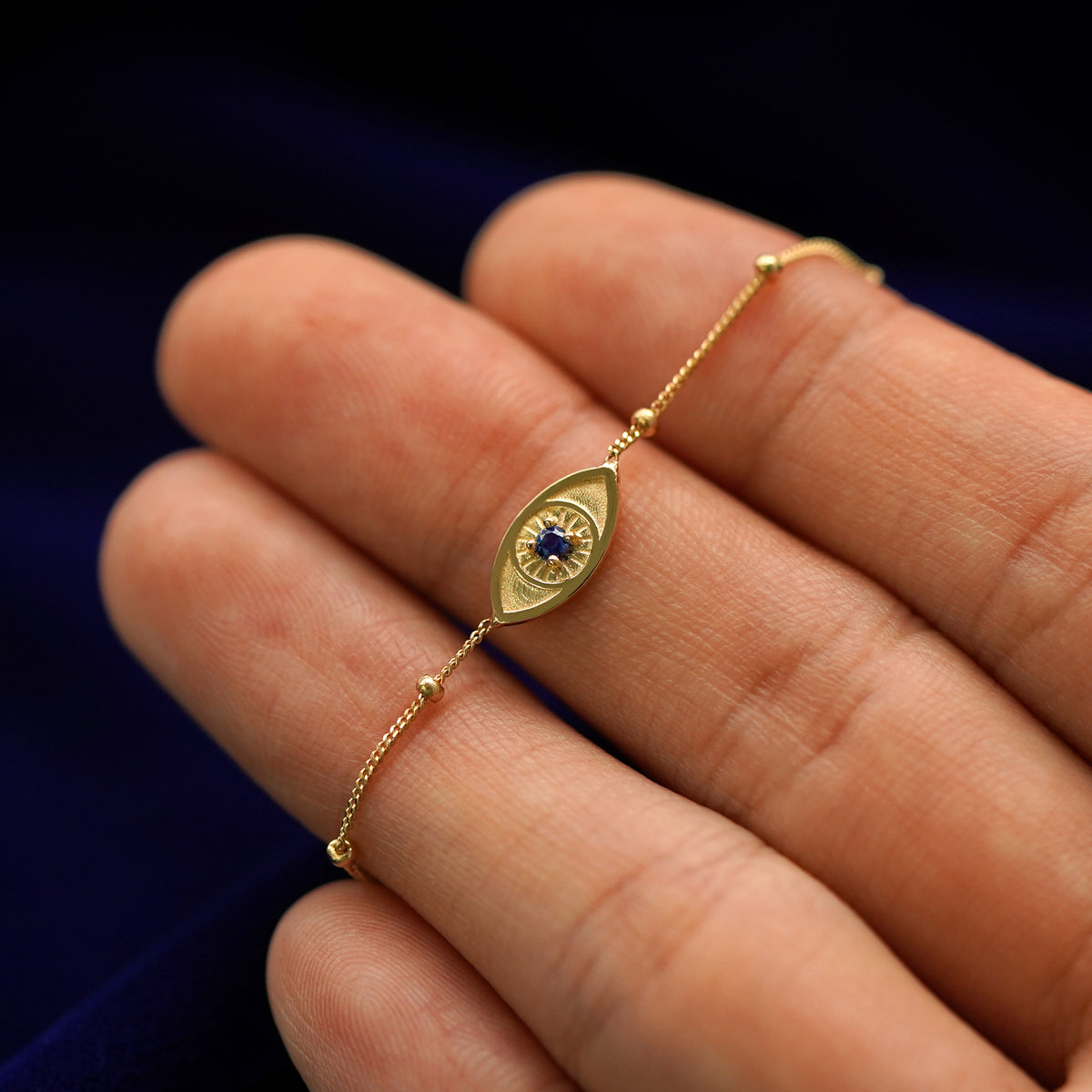 A 14k gold gemstone evil eye bracelet lying across a model's fingertips