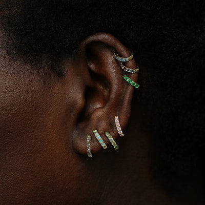 A model wearing multiple gemstone huggie hoops in several lobe and cartilage piercings