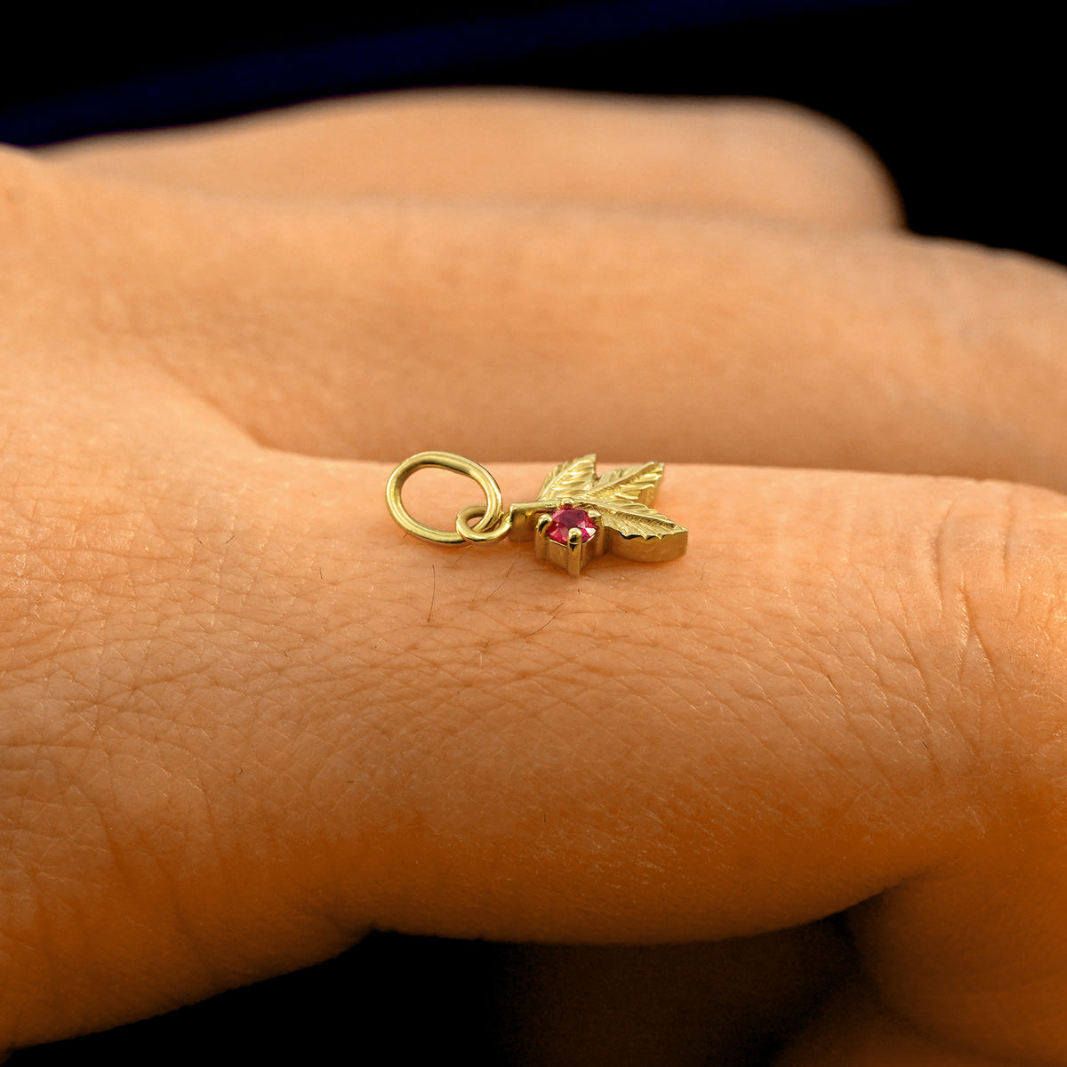 Side view of a 14k solid gold ruby Gemstone 3 Leaves Charm on a model's finger to show the details and thickness of the charm