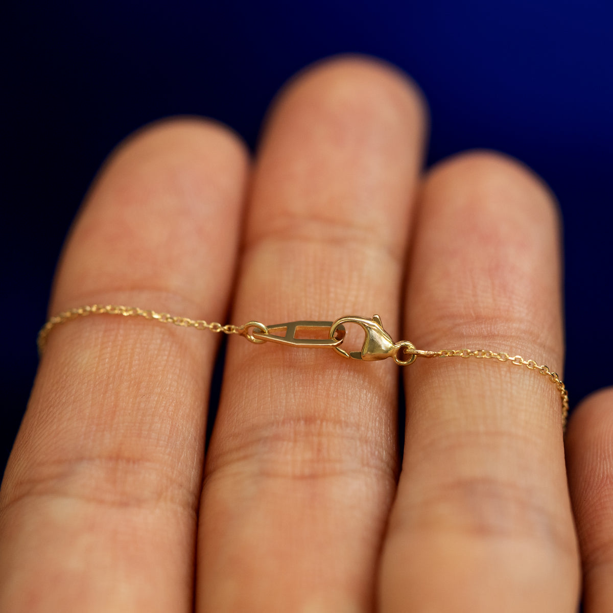 A pink sapphire bezel set gemstone necklace laying over a models fingers to show the clasp on the cable chain