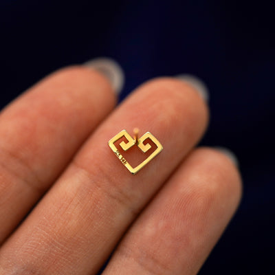 A yellow gold Chere Heart Earring laying facedown on a model's fingers to show the underside view